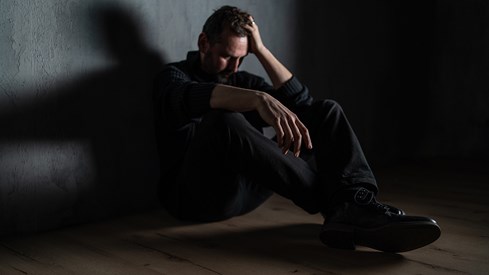 En mann sitter på gulvet med en hånd mot hodet tydelig lei seg