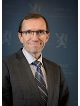 Utenriksminister Espen Barth Eide smilende i dress med blå bakgrunn 