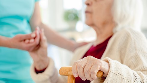 Eldre kvinne blir hjulpet av en anonym hjelpepleier i blått antrekk