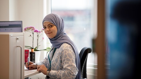 Kvinne med hijab sitter foran pulten på kontor