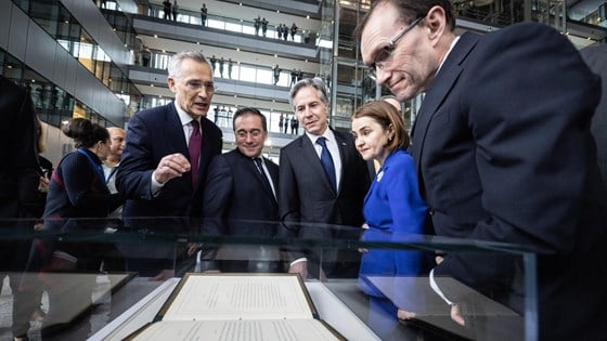 Bilde av fem personer som studerer dokument som ligger i et glassmonter foran dem. 