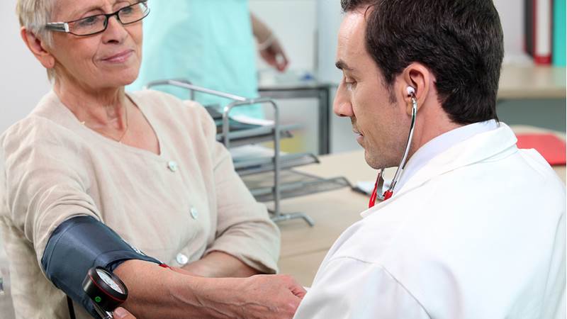 En mannlig lege måler blodtrykket til en eldre kvinnelig pasient