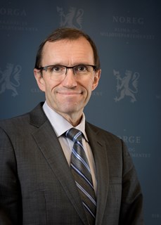 Utenriksminister Espen Barth Eide smilende i dress med blå bakgrunn 
