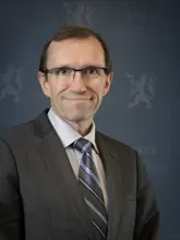 Utenriksminister Espen Barth Eide smilende i dress med blå bakgrunn