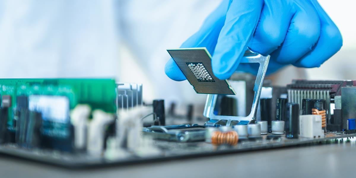 Bilde av en hånd med latexhanske som setter en cpu på et hovedkort.