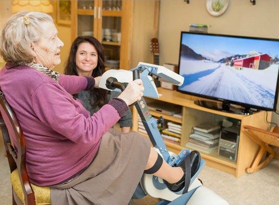 Eldre dame sykler på ergometersykkel og ser på sykkelturen på ein skjerm.
