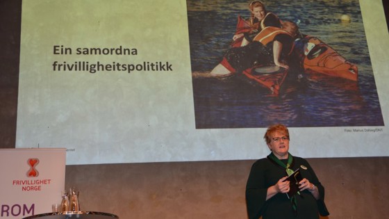Kulturministeren på scenen med powerpoint på storskjerm om frivilligheitsmeldinga bak seg.