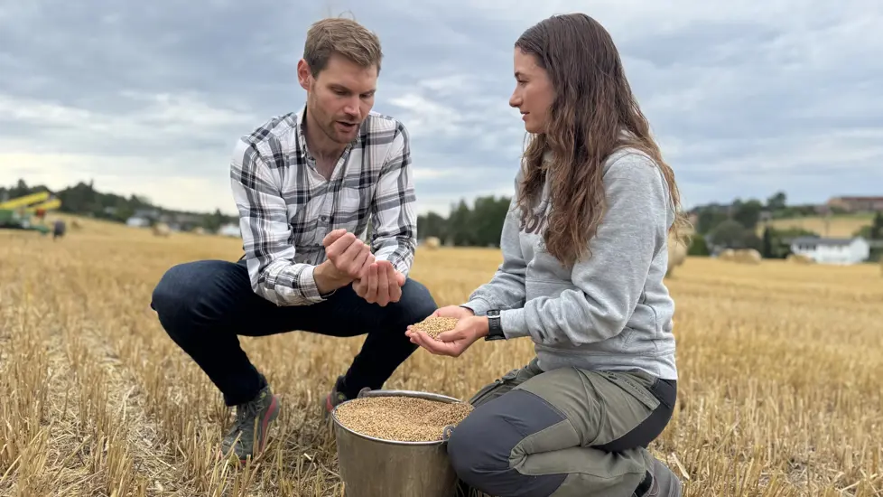 Landbruks- og matminister Nils Kristen Sandtrøen møter kornprodusent Nathalie Bjørneby. Begge sitter på huk i en åker med en kornbøtte mellom seg.