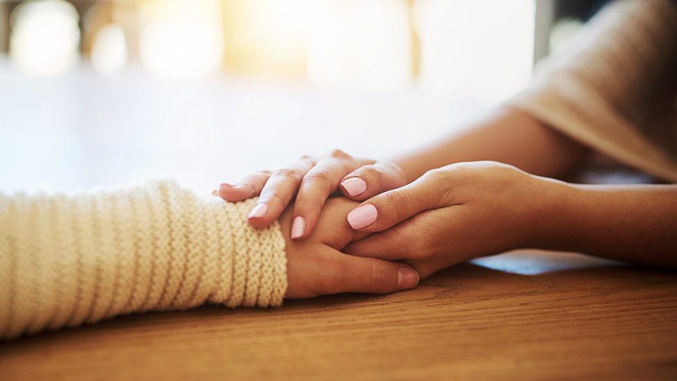 Nærbilde av et par hender som holder over en annen persons ene hånd på en støttende og varm måte