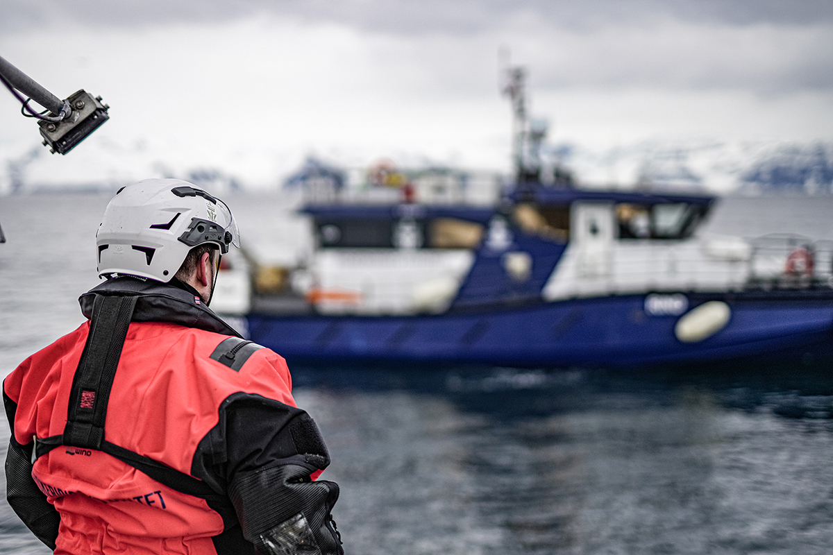 Figur 2.6 Inspektør frå Fiskeridirektoratets sjøteneste om bord ein reketrålar med kontrollfartøyet til sjøtenesta «Rind» i bakgrunnen.