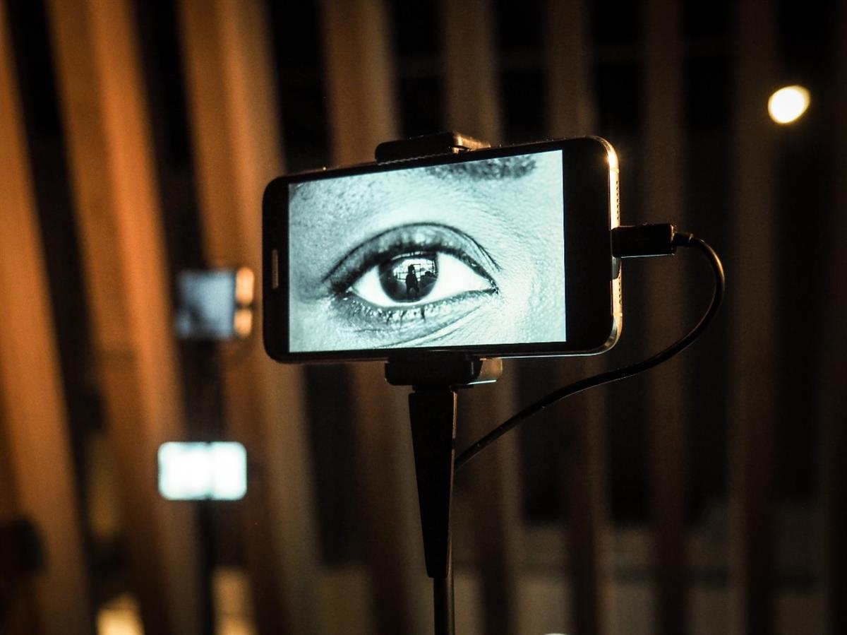 Ghosthouse by the international artist h.o. A black and white image of a human eye on a mobile screen mounted on a pole. There are more such screens glowing in the background. Used with permission from Ars Electronica and Martin Hieslmair.