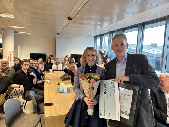 Bilete viser Bjørn Haugstad, direktør for organisasjon og infrastruktur, som på vegner av NTNU fekk overrekt prisen frå statsråd Karianne Tung. Bak dei to sit ei forsamling av tilsette og lærlingar ved NTNU.