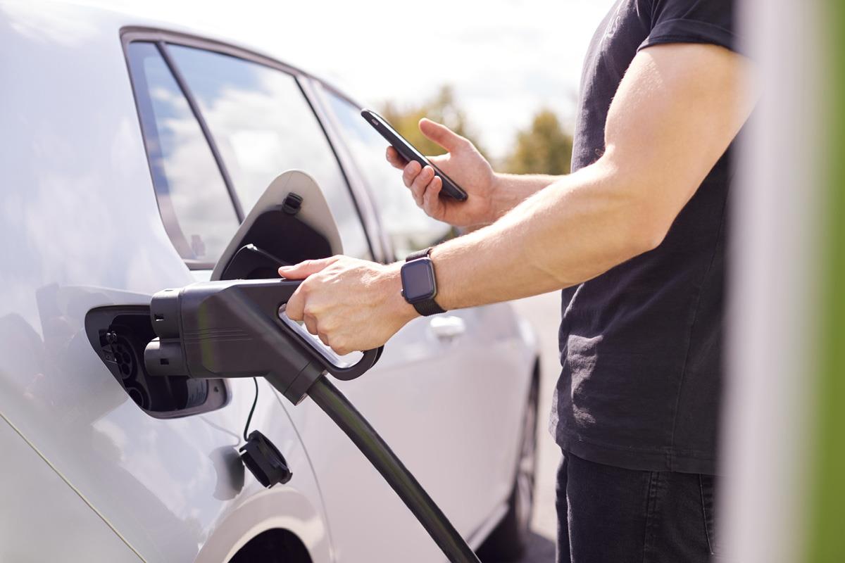 Illustration photo. Man charging a car while interacting with a phone.
