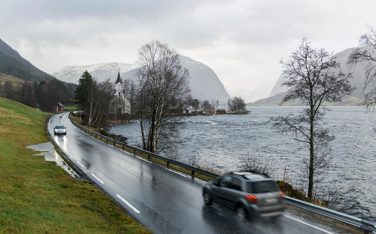 Illustration photo. Cars driving on a road along some water.