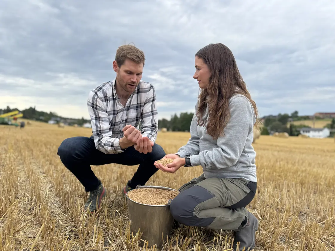 Landbruks- og matminister Nils Kristen Sandtrøen møter kornprodusent Nathalie Bjørneby. Begge sitter på huk i en åker med en bøtte med korn mellom seg.