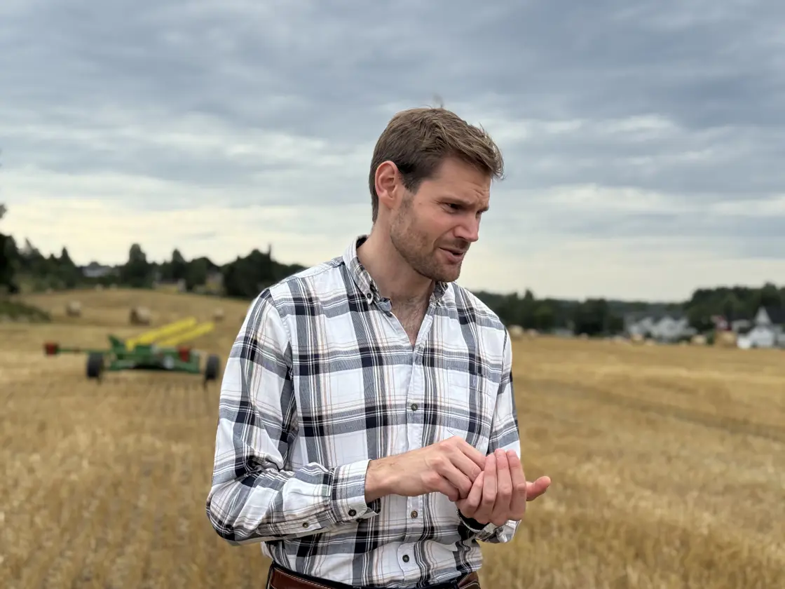 Landbruks- og matminister Nils Kristen Sandtrøen besøker kornprodusent. Ministeren står på en åker med korn i hånden.
