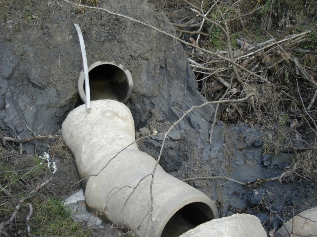 Bilde fra Asplan Viak-rapport, med bildeteksten «Utglidning av leirmasser i bekkeløp i felt I med OV-rørkollaps. Bekken graver direkte i leire.» (Asplan Viak, 2009).