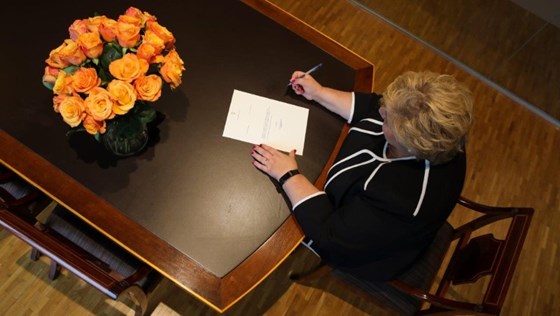 Statsminister Erna Solberg sitter ved et bord og skriver under på regjeringens avskjedssøknad.
