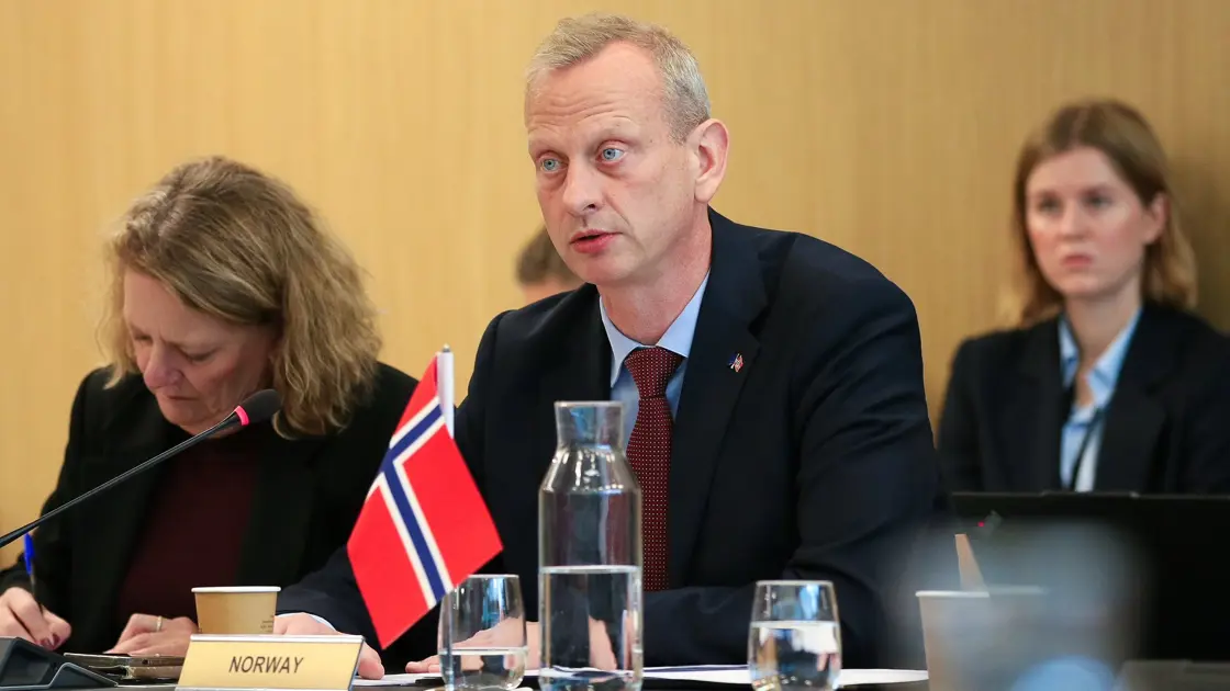 En mann i dress med et norsk bordflagg foran seg.