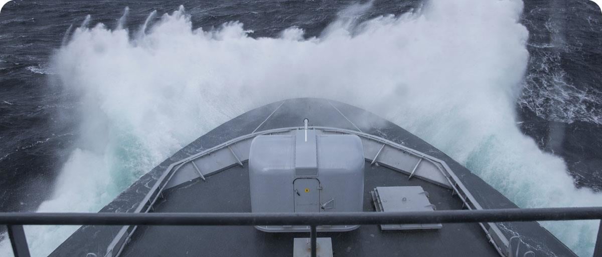 The sea spray rises around the bow of a coast guard vessel in rough seas.
