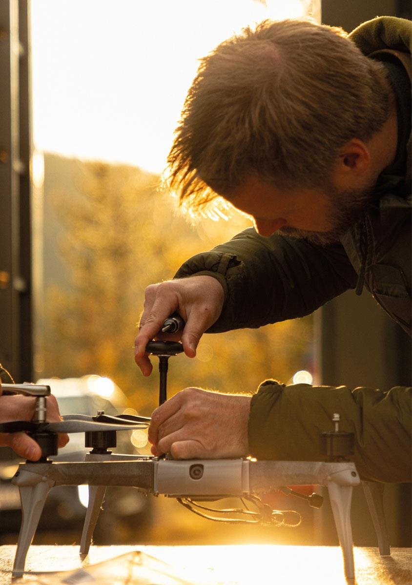 En soldat står innendørs, bøyd over en liten helikopterdrone med en skrutrekker.