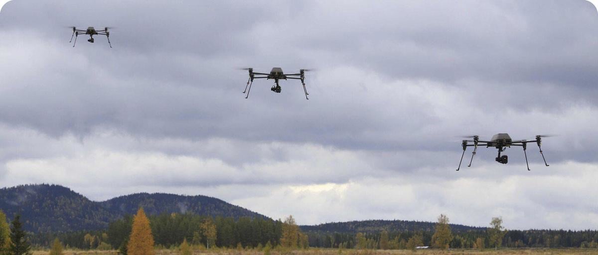 Tre helikopter-droner i luften. De ligger på linje skrått diagonalt i bildet.