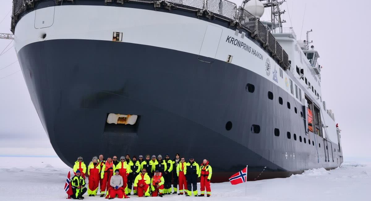 The research ship Kronprins Haakon breaks the ice, with the crew lined up in front of the bow.