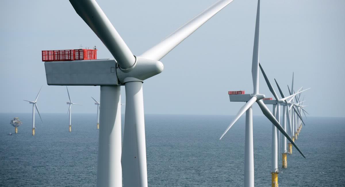 En samling av store vindturbiner stående på rekke langt ute i havet.