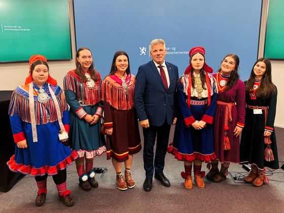 De samiske veiviserne stiller opp i tradisjonelle kofter sammen med statsråden som stiller i blå dress