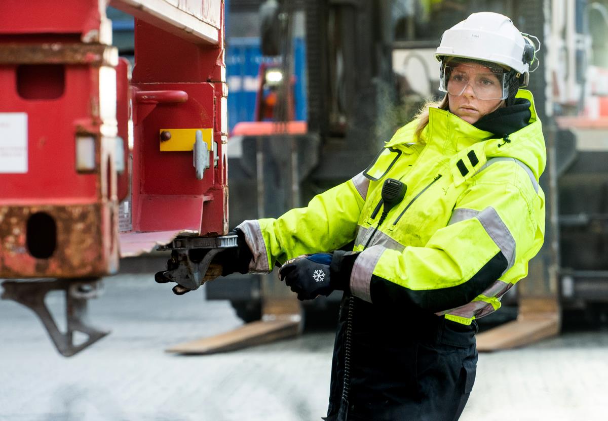 A woman wearing work clothes, helmet and protective glasses at work