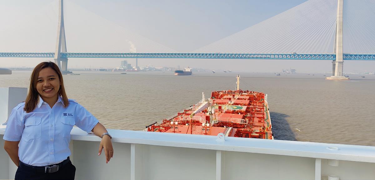 A female seafarer on board a large vessel sailing towards a bridge seen in the background
