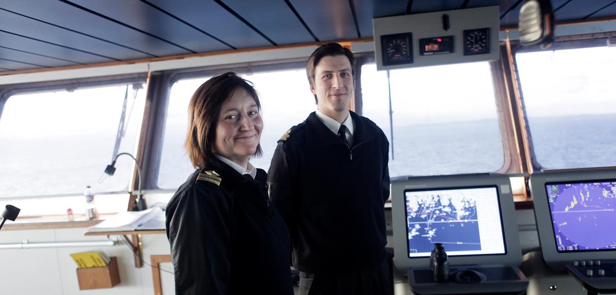 Two seafarers standing on the bridge of a ship with navigation equipment visible in the background