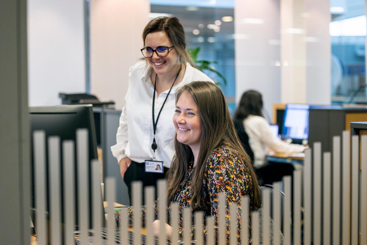 Two smiling women behind a computer screen in an office