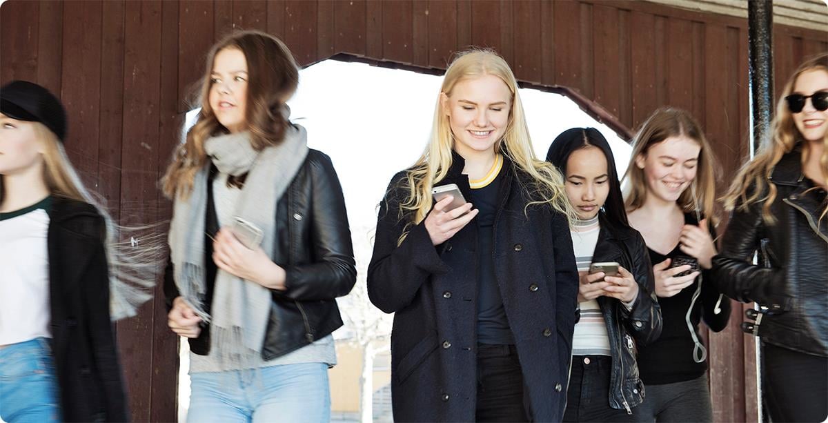 Flere jenter i en skolegård med telefoner i hendene.