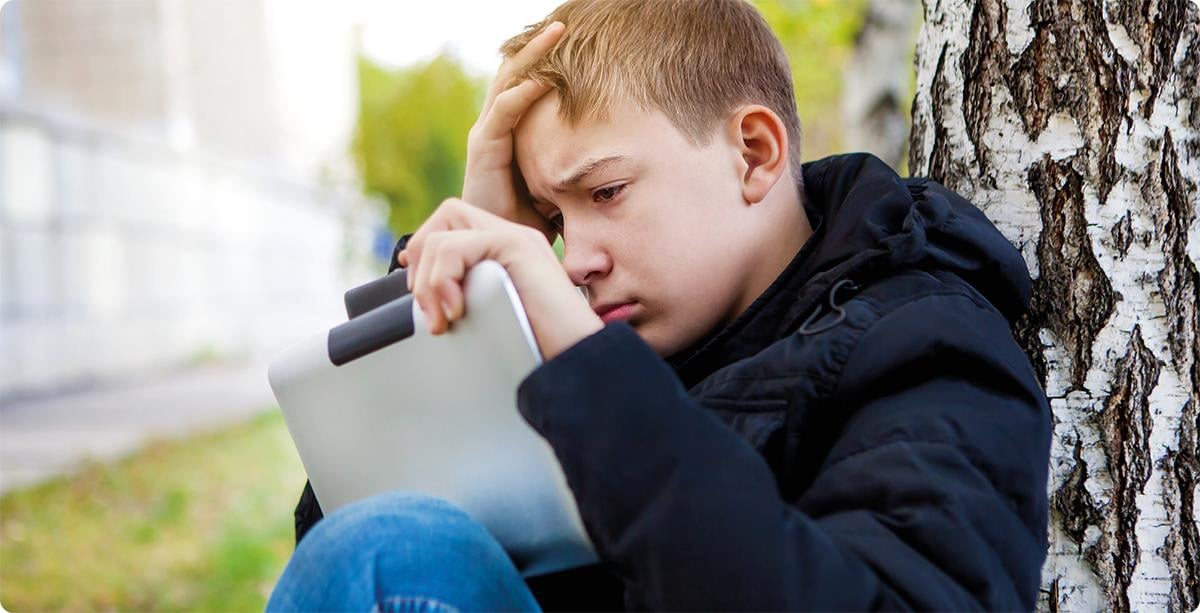 Bekymret gutt lent mot et tre ser på ipad.