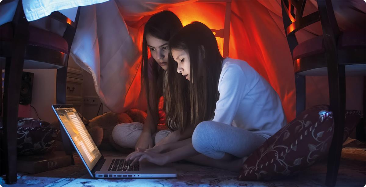 Jenter sitter på gulvet i mørket og ser på PC.