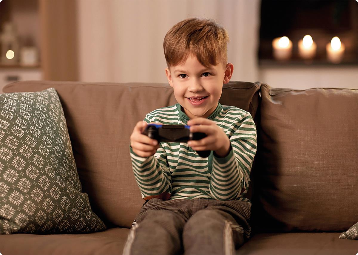 Smilende gutt på sofa med spillkontroll.