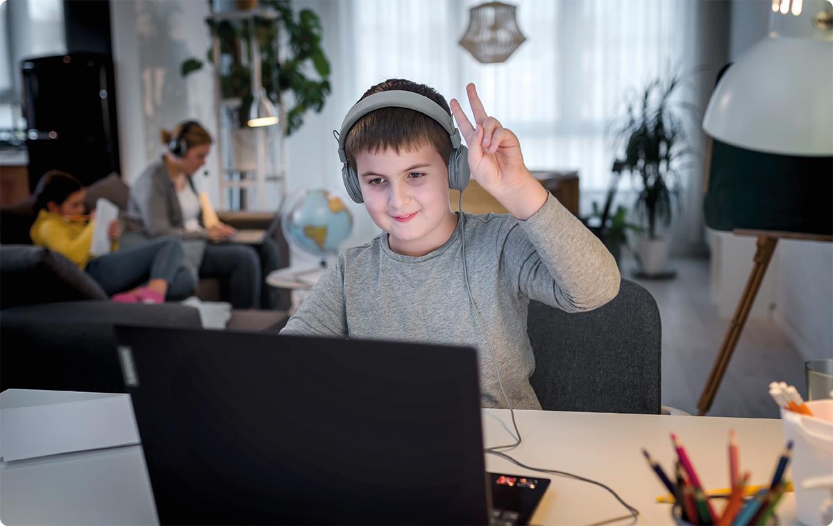 Gutt med headsett ser på bærbar PC og rekker opp hånden.