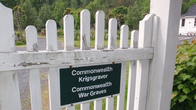 Picture of a white wooden gate at Risør war cemetery with a black sign with the following text: "Commonwealth Krigsgraver / Commonwealth War Graves".