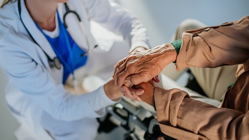 En sykepleier og en eldre person holder hender