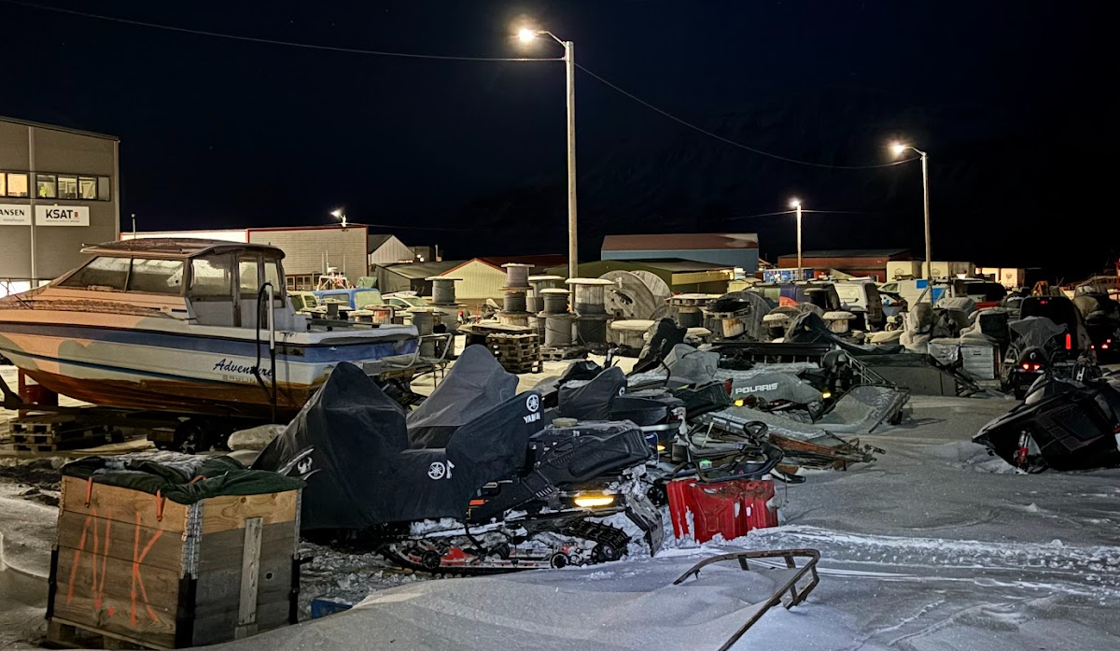 Bildet viser flere snøskutere, biler og en båt som står i snøen