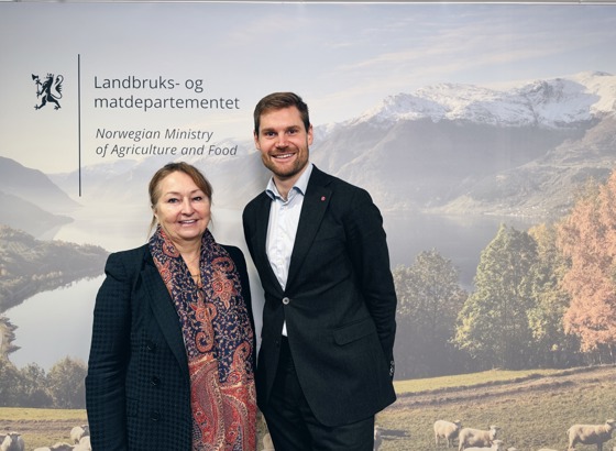 Landbruks- og matministeren sammen med styreleder i KS. Bakgrunn er fotovegg hos Landbruks- og matdepartementet.