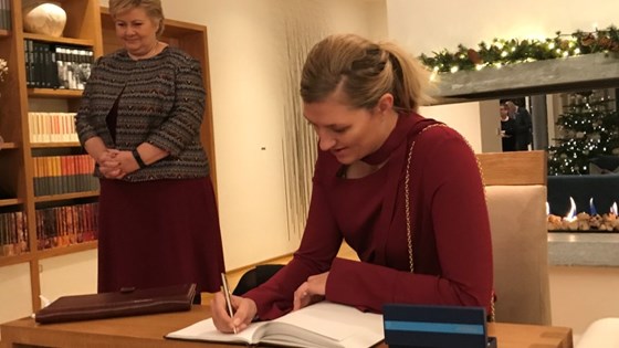 Beatrice Fihn skriver i gjesteboken i statsministerboligen. Statsminister Erna Solberg står bak henne.