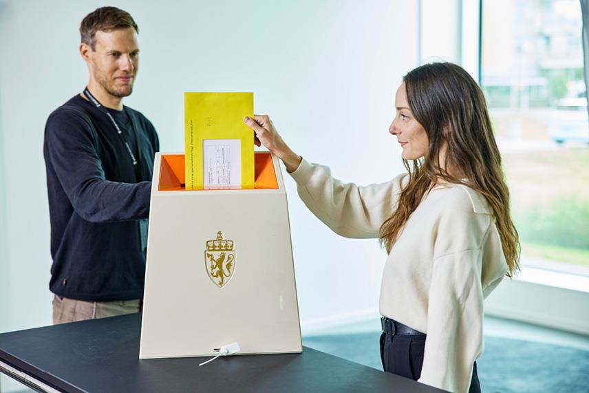 Foto som viser en velger som legger omslagskonvolutten i urnen.