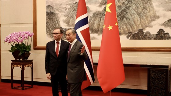 Bilde av utenriksminister Eide og Kinas utenriksminister Wang Yi stående foran flagg