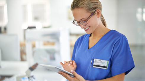 Sykepleier i blå uniform smiler og ser på en iPad