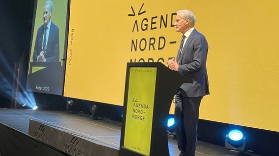 Statsminister Jonas Gahr Støre står på scenen foran en gul vegg. Han har på seg dress, og støtter seg til en talerstol.
