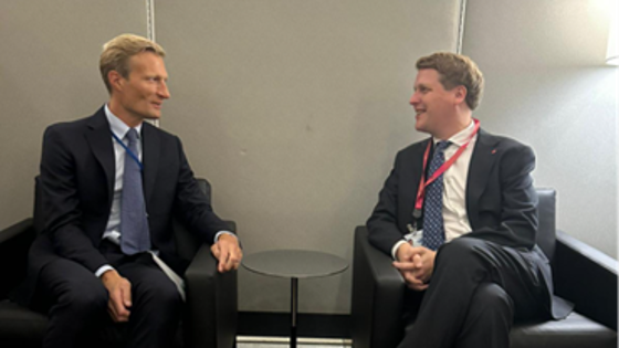 To menn i dress bak et bord