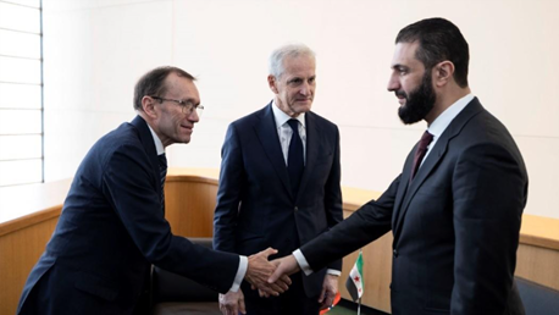 Tre menn i dress hvorav to som hilser på hverandre