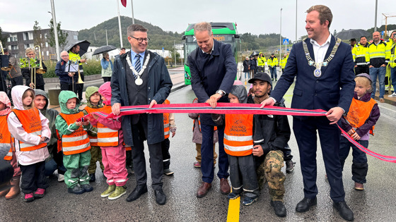 En gruppe barnehagebarn deltar ved snorklipping for en veiåpning, sammen med en gruppe voksne personer.